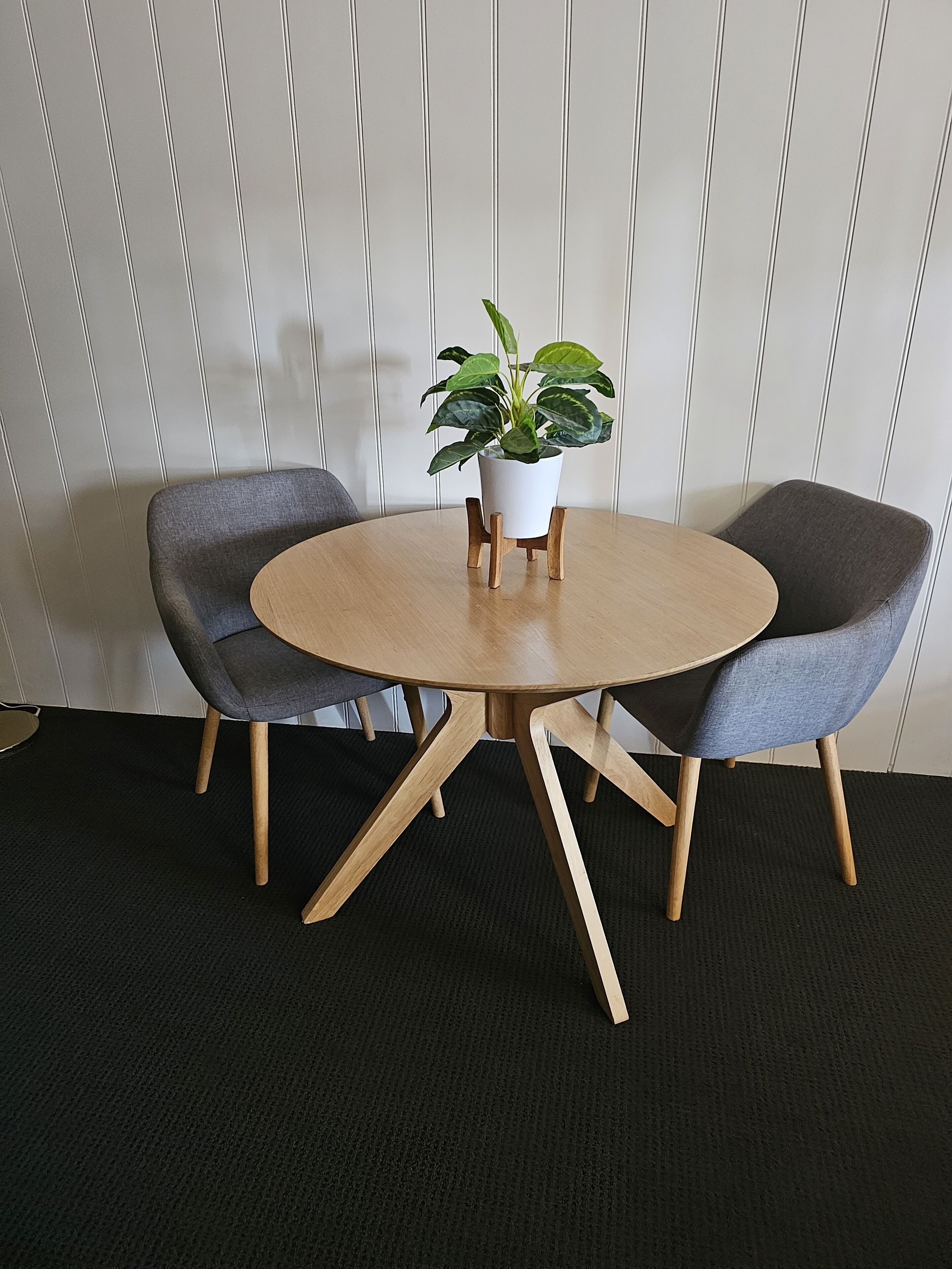 A round table with a potted plant in the center, flanked by two grey upholstered chairs with wooden legs.
