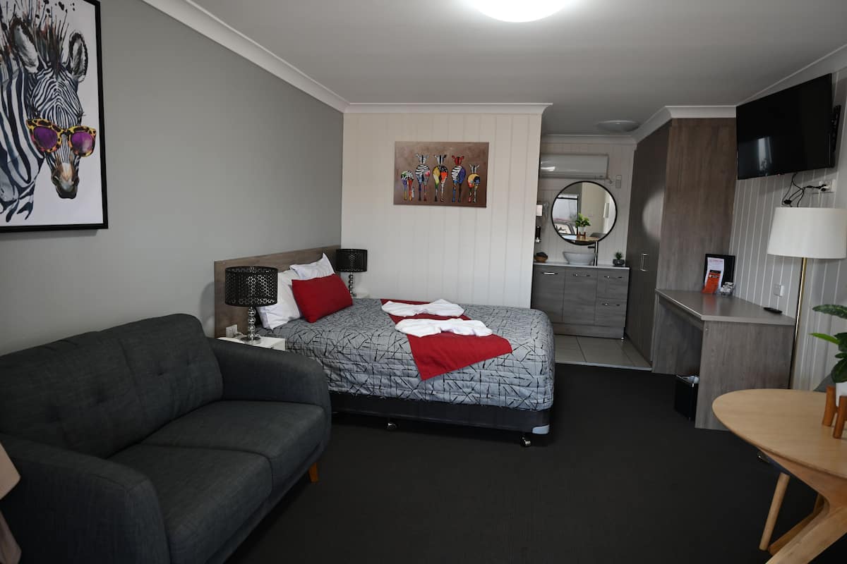 Ett modernt hotellrum med en säng, en soffa, ett skrivbord, en tv och ett badrum som syns i bakgrunden.