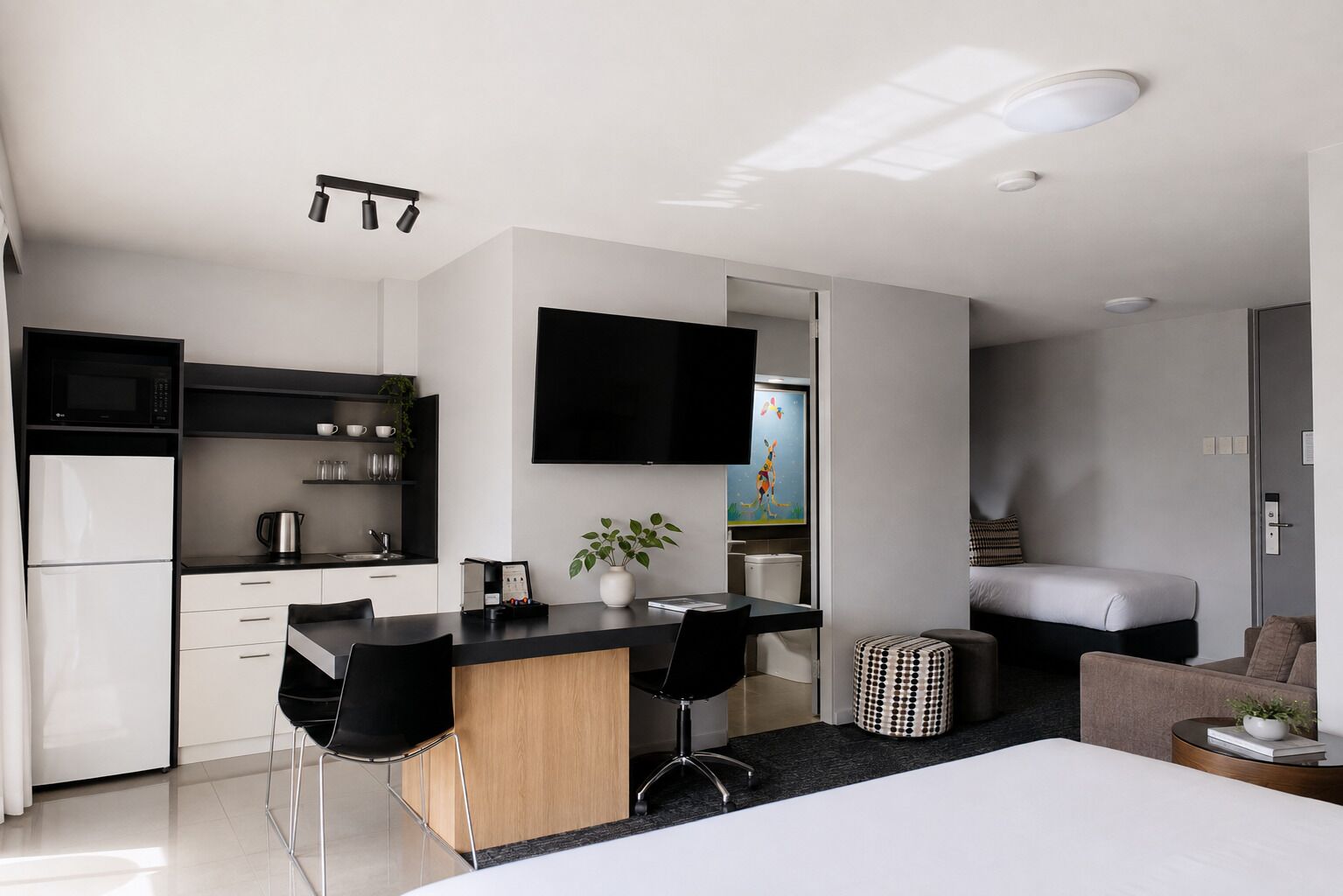 A modern kitchen with a black countertop, white cabinets, and a flat-screen TV mounted above the counter.