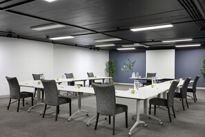 Een vergaderruimte met witte tafels, grijze stoelen en een projectorscherm.