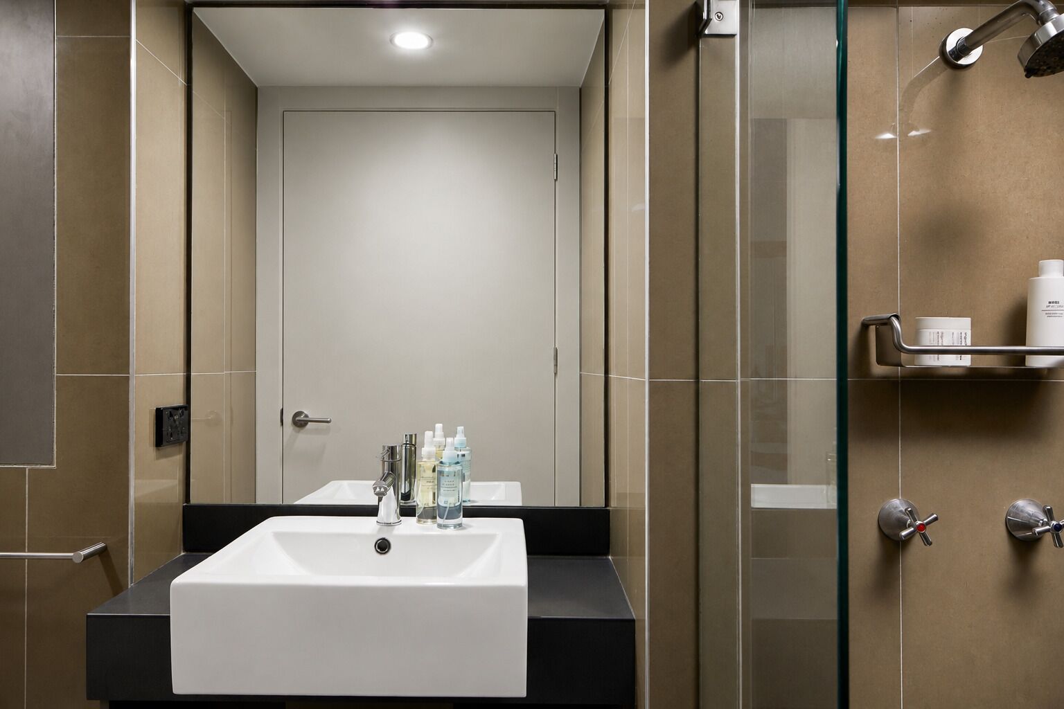 A modern bathroom with a white sink, a glass shower enclosure, and a shelf with toiletries.