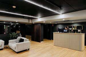 Una moderna zona de recepción con mostrador, un área de descanso con dos sofás y suelo de madera.