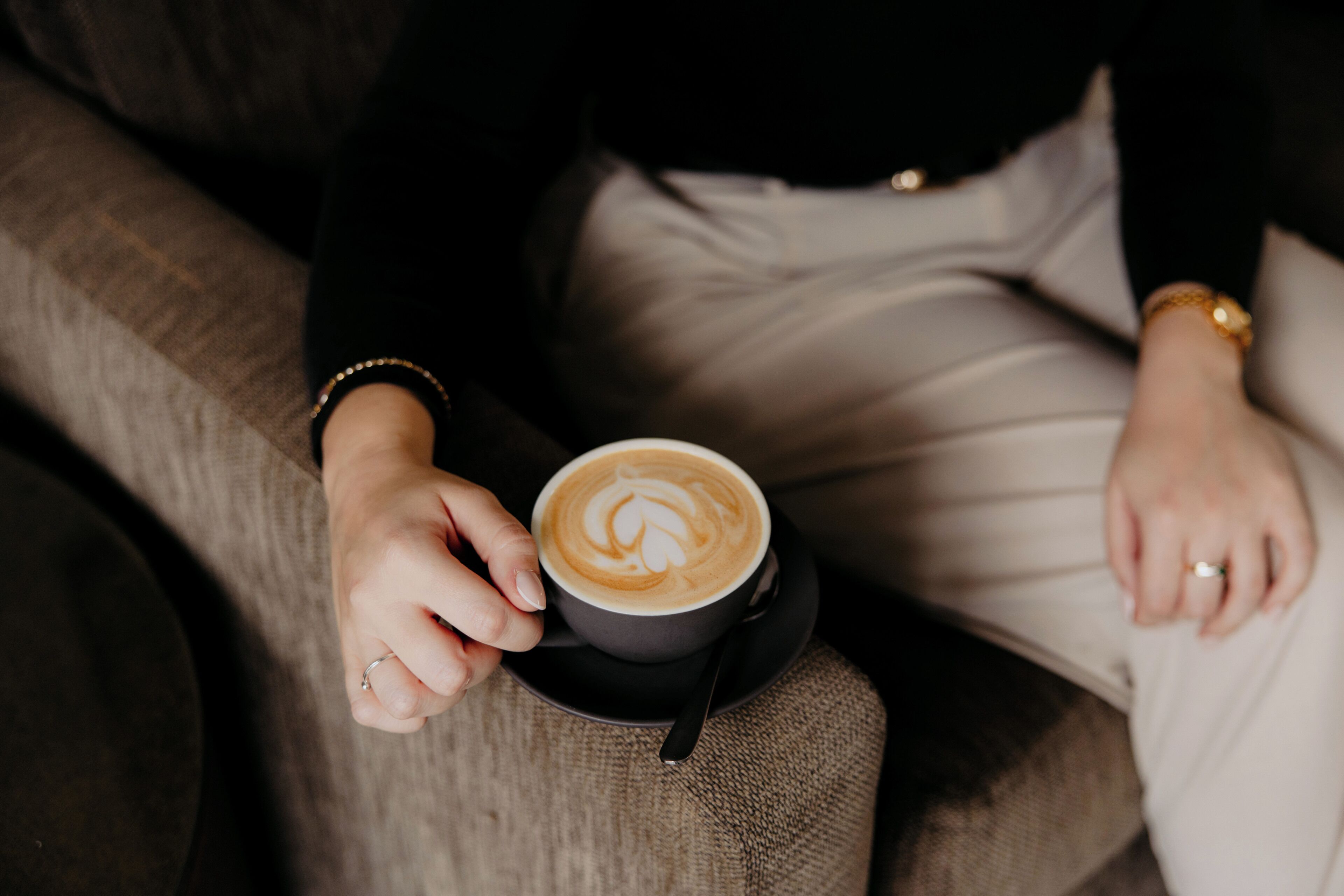 Eine Person hält eine Kaffeetasse und sitzt auf einem Sofa.