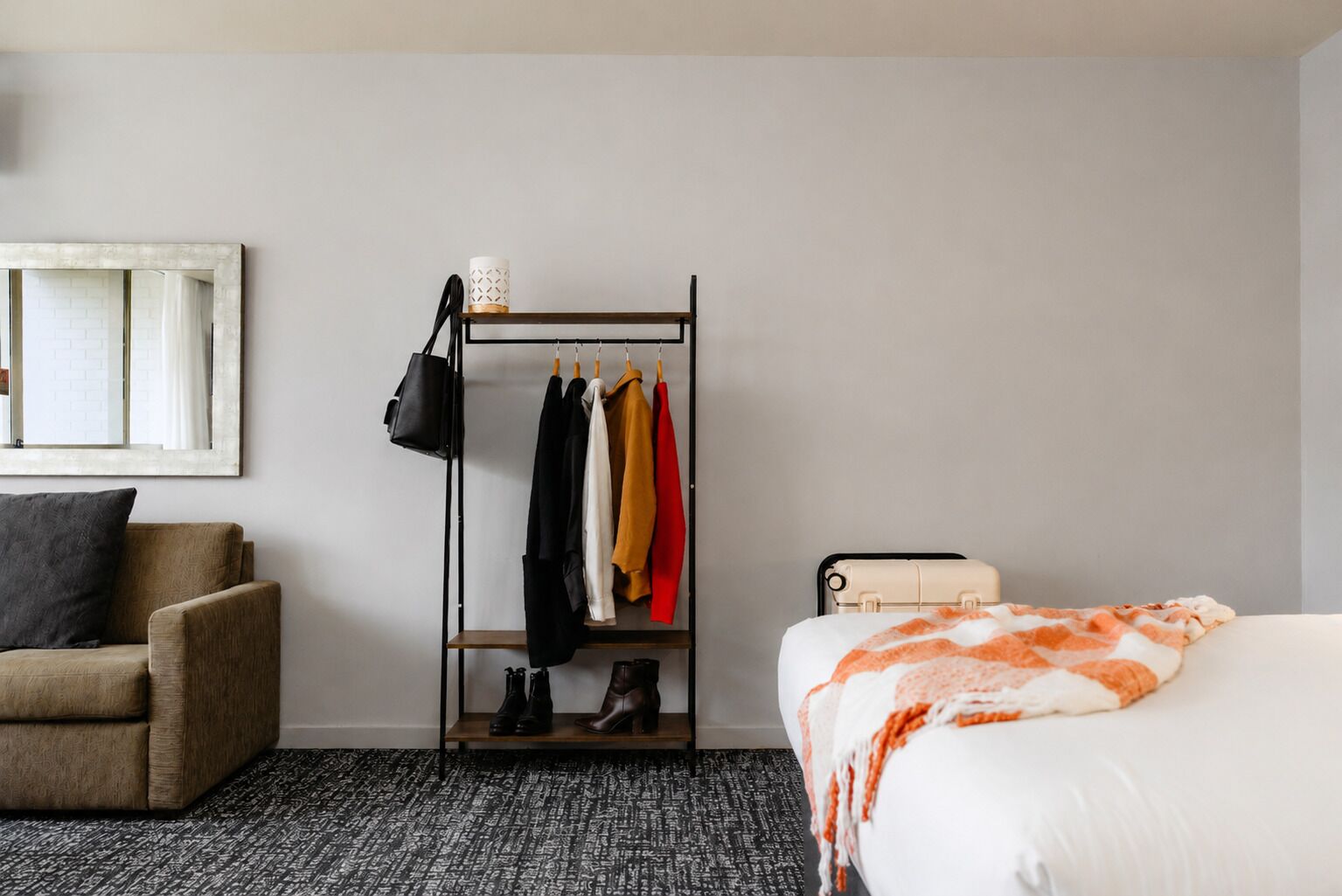 Una camera d'albergo con un letto, una sedia, un appendiabiti e un tavolino.