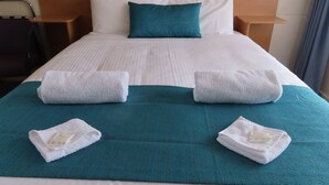 A neatly made bed with white linens, teal pillows, and two towels with soap labels. - Ceduna East West Motel (Ceduna)