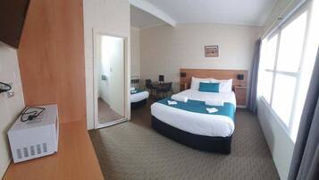A hotel room with a large bed, a desk, and a chair. There is a mirror on the wall and a window with curtains.