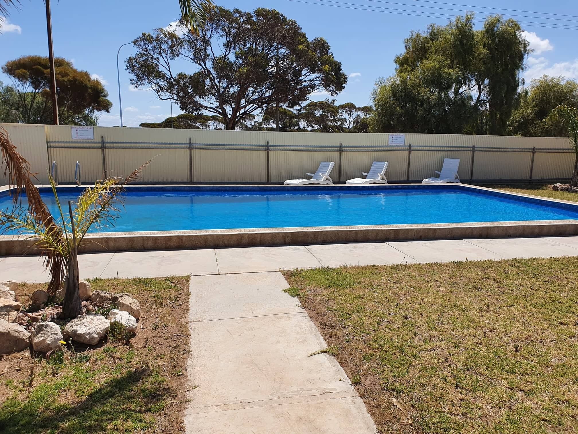 Una piscina rettangolare con bordo in cemento e un vialetto lastricato che vi conduce.