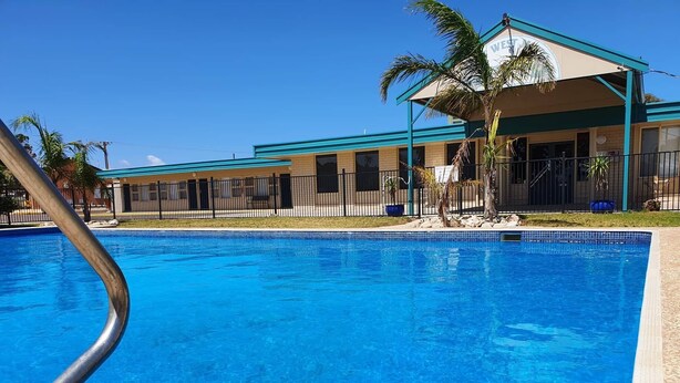 A swimming pool with a metal ladder, surrounded by a fence and palm trees. - Ceduna East West Motel (Ceduna)