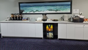 A hotel bar area with a large flat-screen TV displaying a beach scene, a refrigerator stocked with beverages, and various bar amenities. - Ceduna East West Motel (Ceduna)