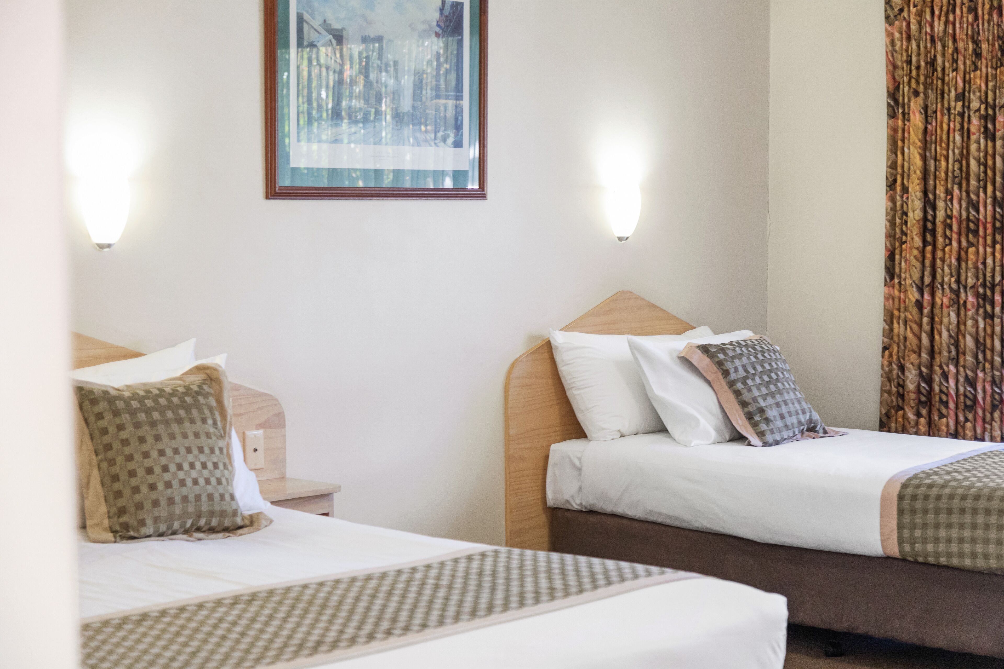 A hotel room with two beds, a framed artwork on the wall, and a curtain on the window.