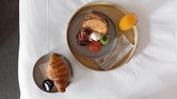 A breakfast tray with toast, bacon, eggs, avocado, and a glass of orange juice on a white tablecloth.
