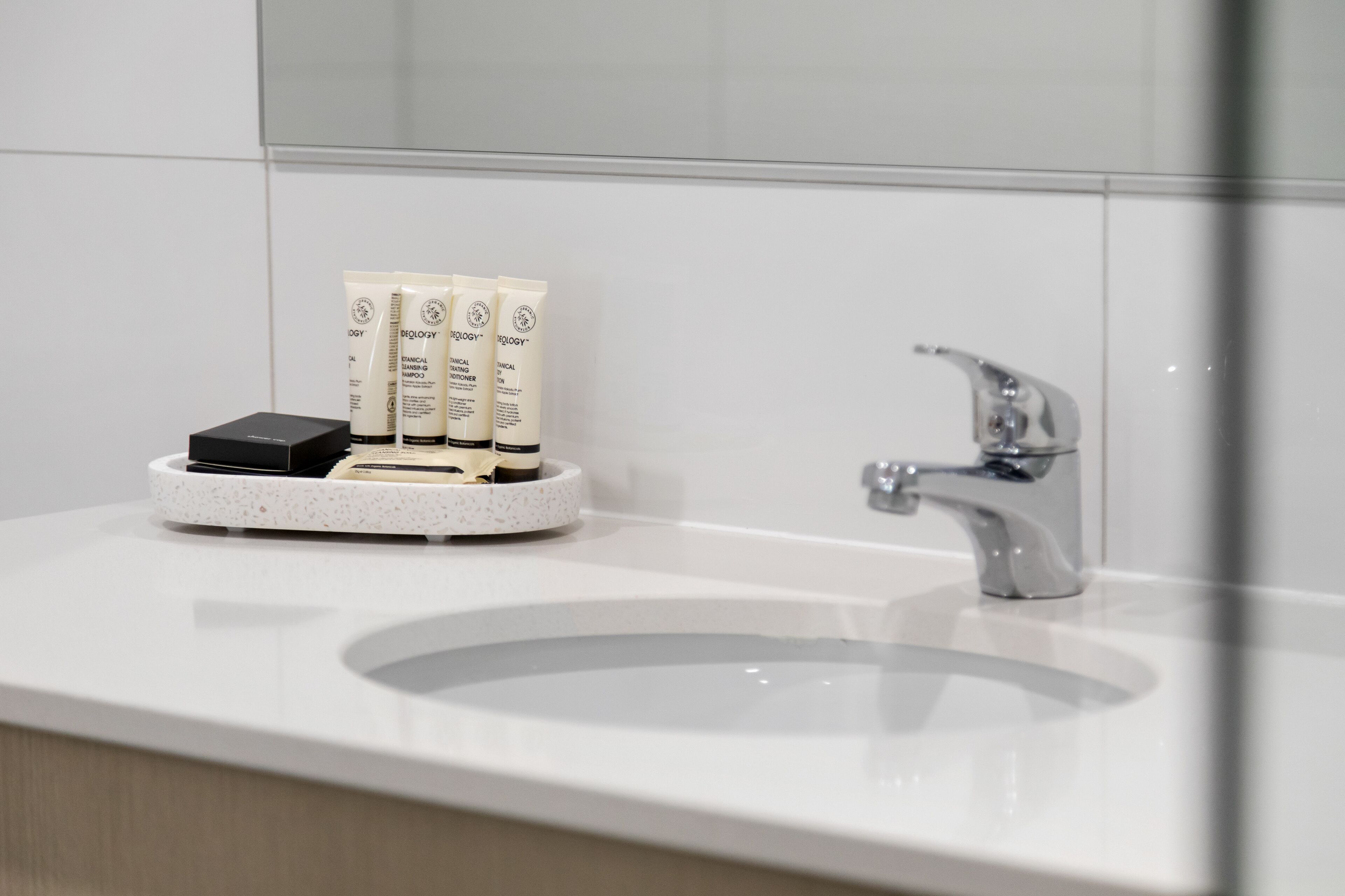 Un baño moderno con un lavamanos blanco, un grifo cromado y tres botellas de tocador sobre una bandeja.