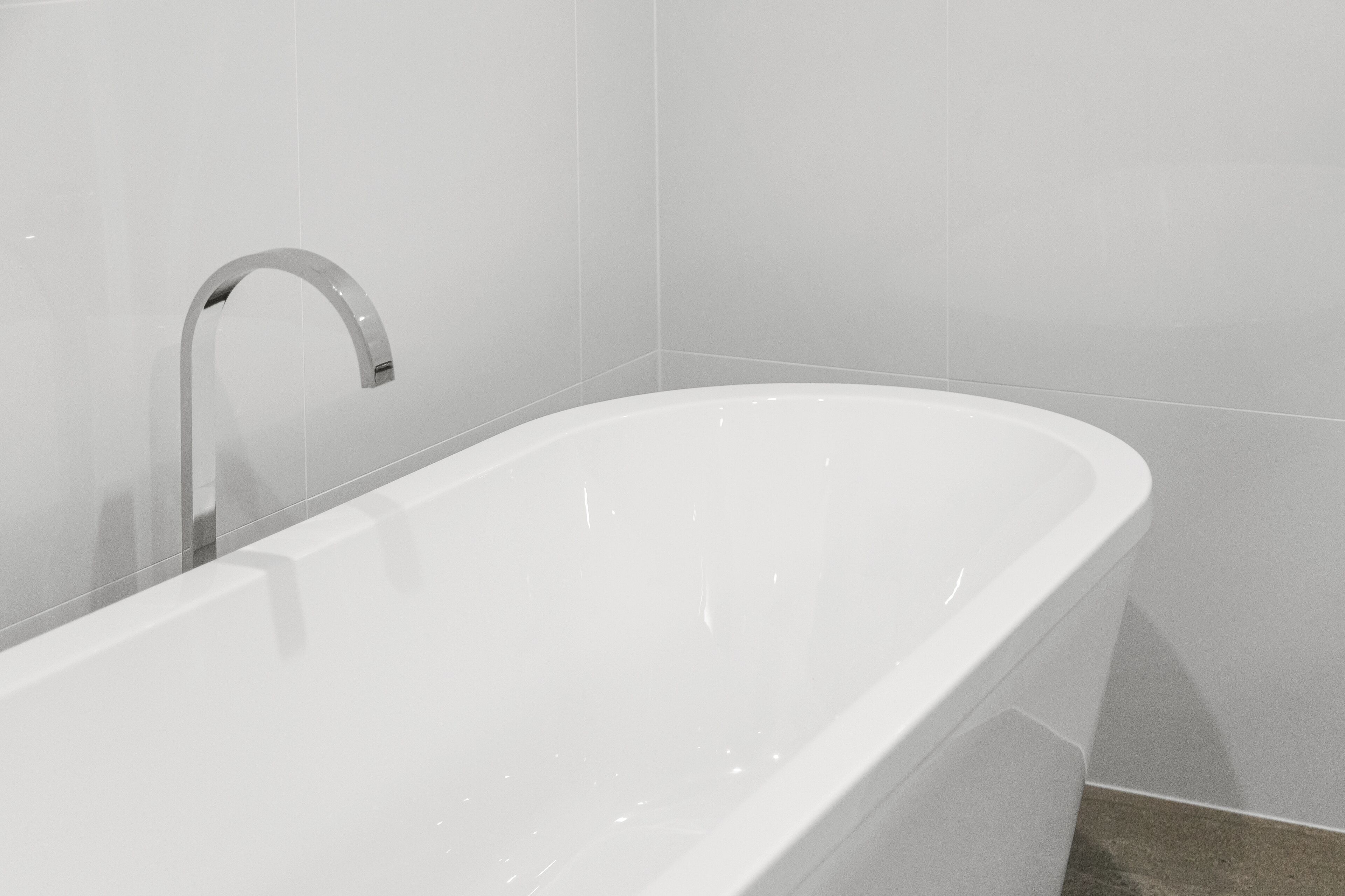 A modern bathroom with a freestanding bathtub, a chrome faucet, and white tiled walls.