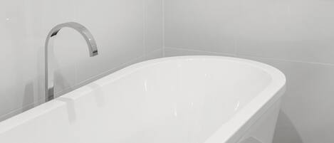 A modern bathroom with a freestanding bathtub, a chrome faucet, and white tiled walls.