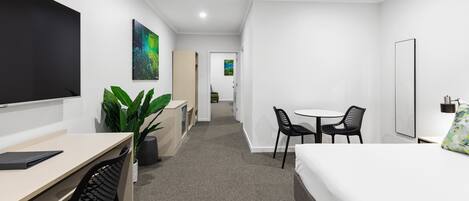 Une chambre d’hôtel moderne équipée d’un lit, d’un bureau, de chaises, d’un téléviseur à écran plat et d’une plante.