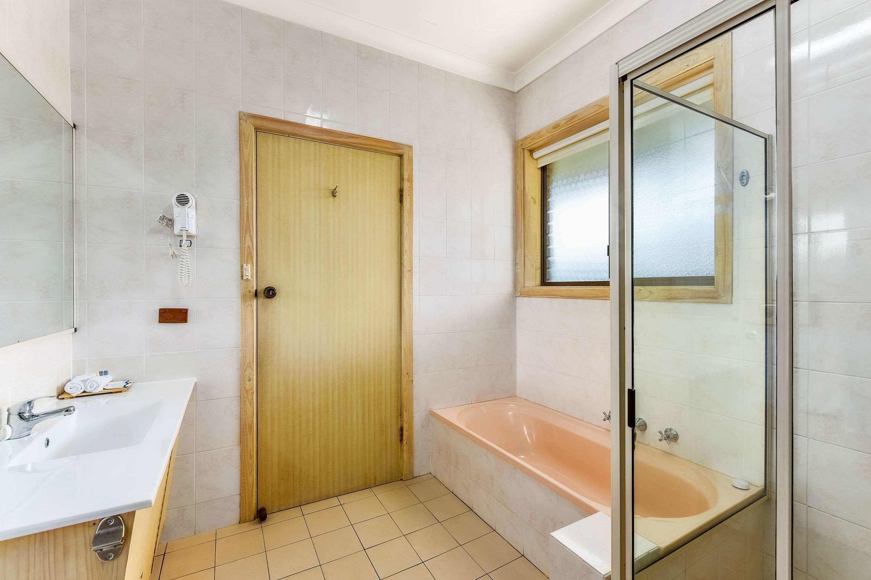 A bathroom with a wooden door, a white sink, a glass-enclosed shower, and a bathtub.