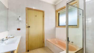 Un baño con puerta de madera, un lavamanos blanco, ducha con mampara de vidrio y una bañera.