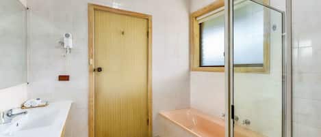 Une salle de bain avec une porte en bois, un lavabo blanc, une douche à parois de verre et une baignoire.