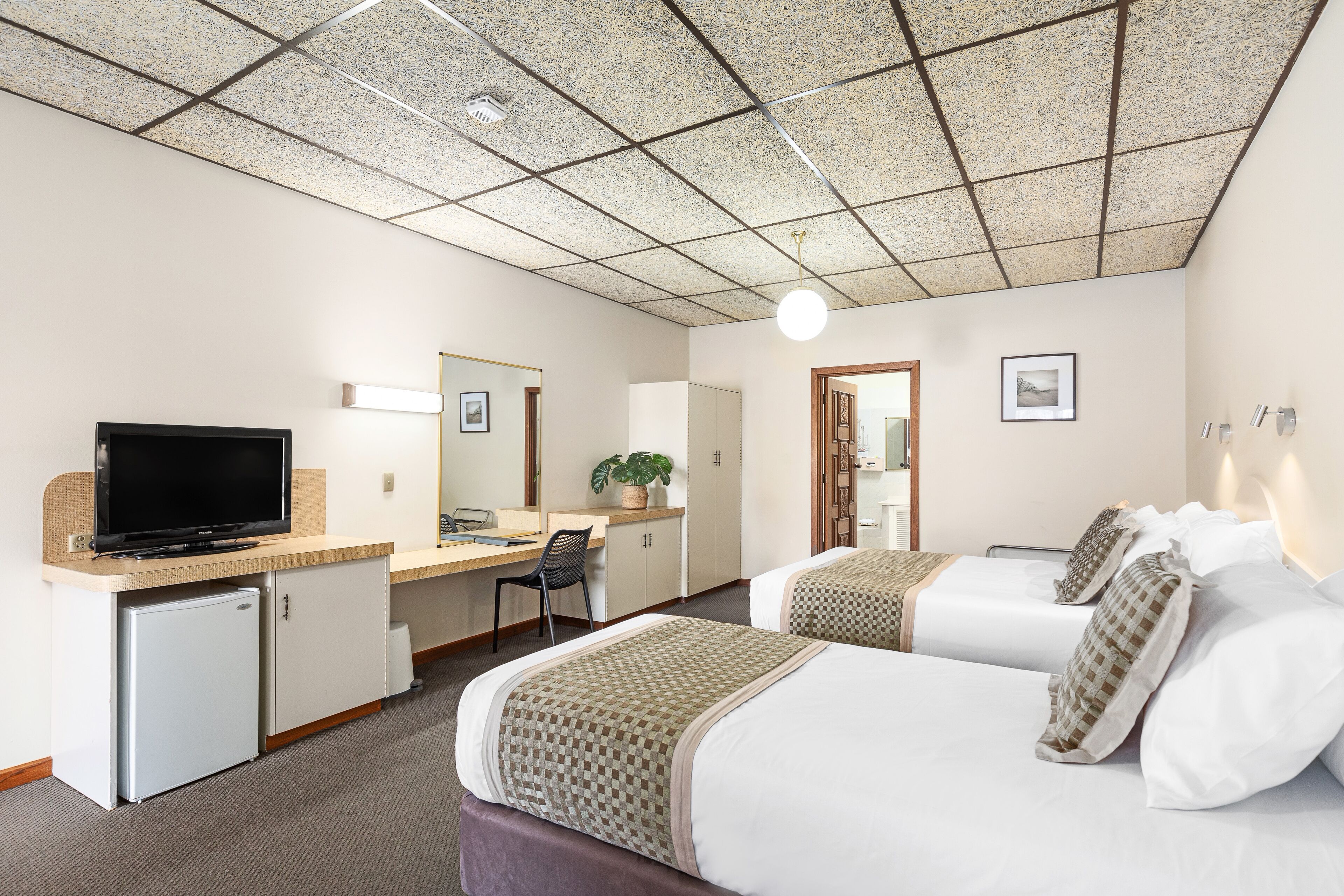 Habitación de hotel con dos camas, un escritorio con televisor, un refrigerador pequeño y un ventanal grande.