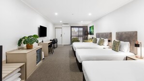 A modern hotel room with three beds, a desk, a chair, a TV, and a plant. - Presidential Motel (Mount Gambier)