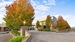 A hotel entrance with a covered parking area, brick landscaping, and autumn-colored trees. - Presidential Motel (Mount Gambier)