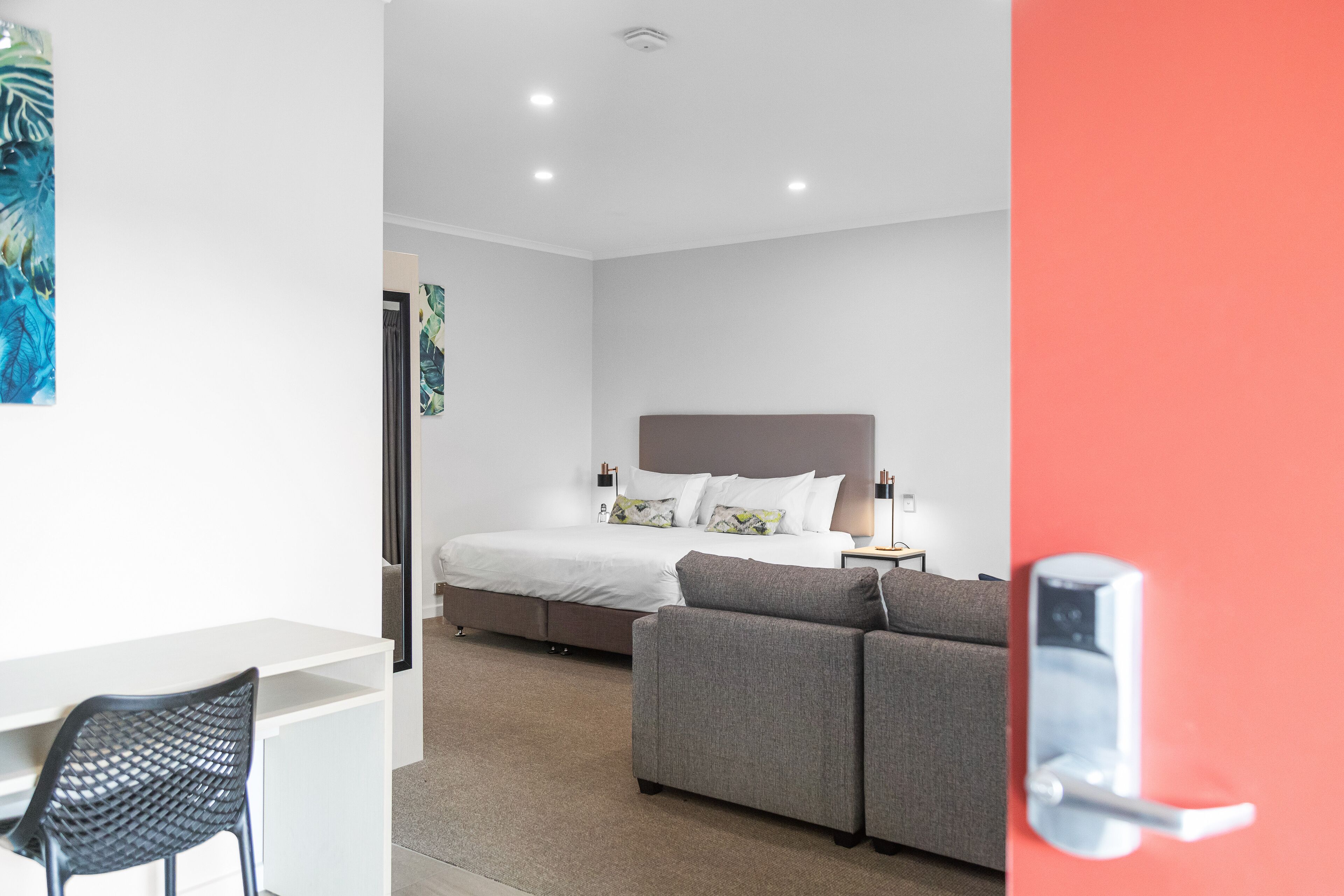 Moderni hotellihuone, jossa on sänky, sohva, työpöytä ja tuoli.