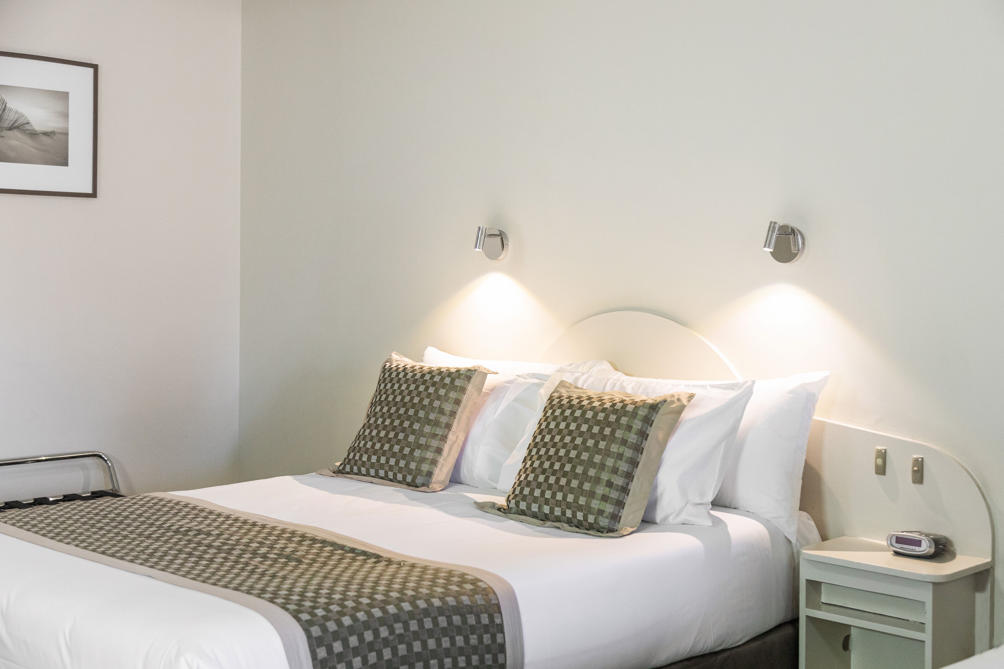 A neatly made bed with patterned pillows and a bedside table with a clock.