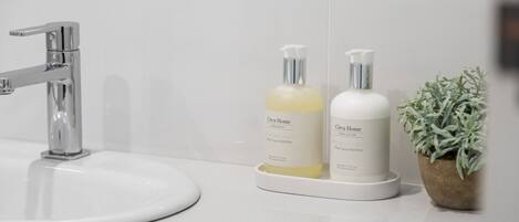 A bathroom sink with a chrome faucet, two bottles of hand wash and lotion, and a potted plant.