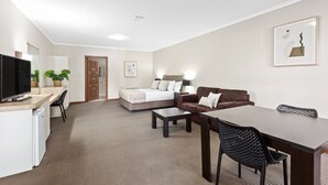 A modern hotel room with a bed, a sofa, a dining table, and a TV. - Presidential Motel (Mount Gambier)