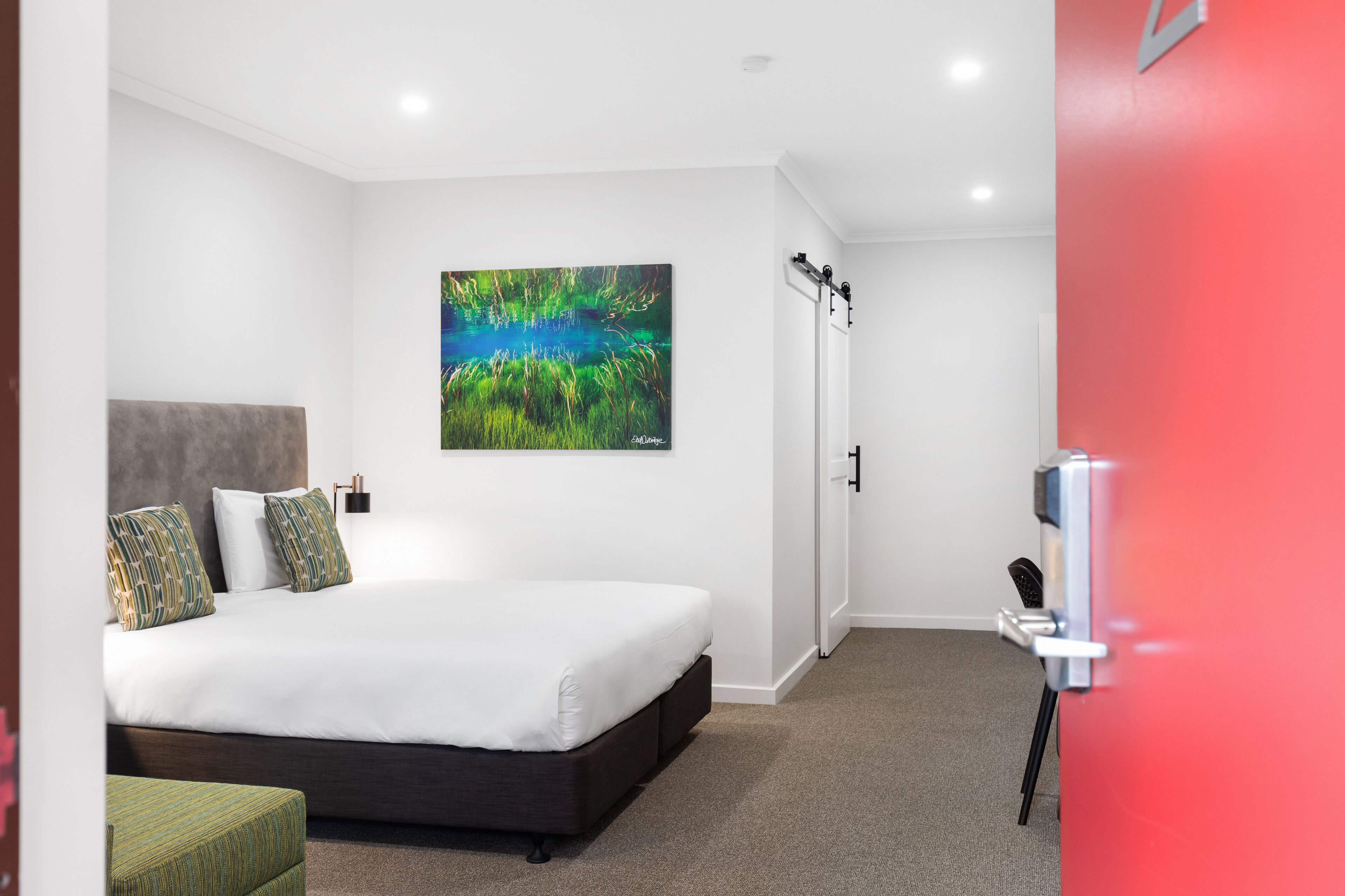 Un dormitorio moderno con una cama grande, un cuadro en la pared y una puerta con cámara de seguridad.