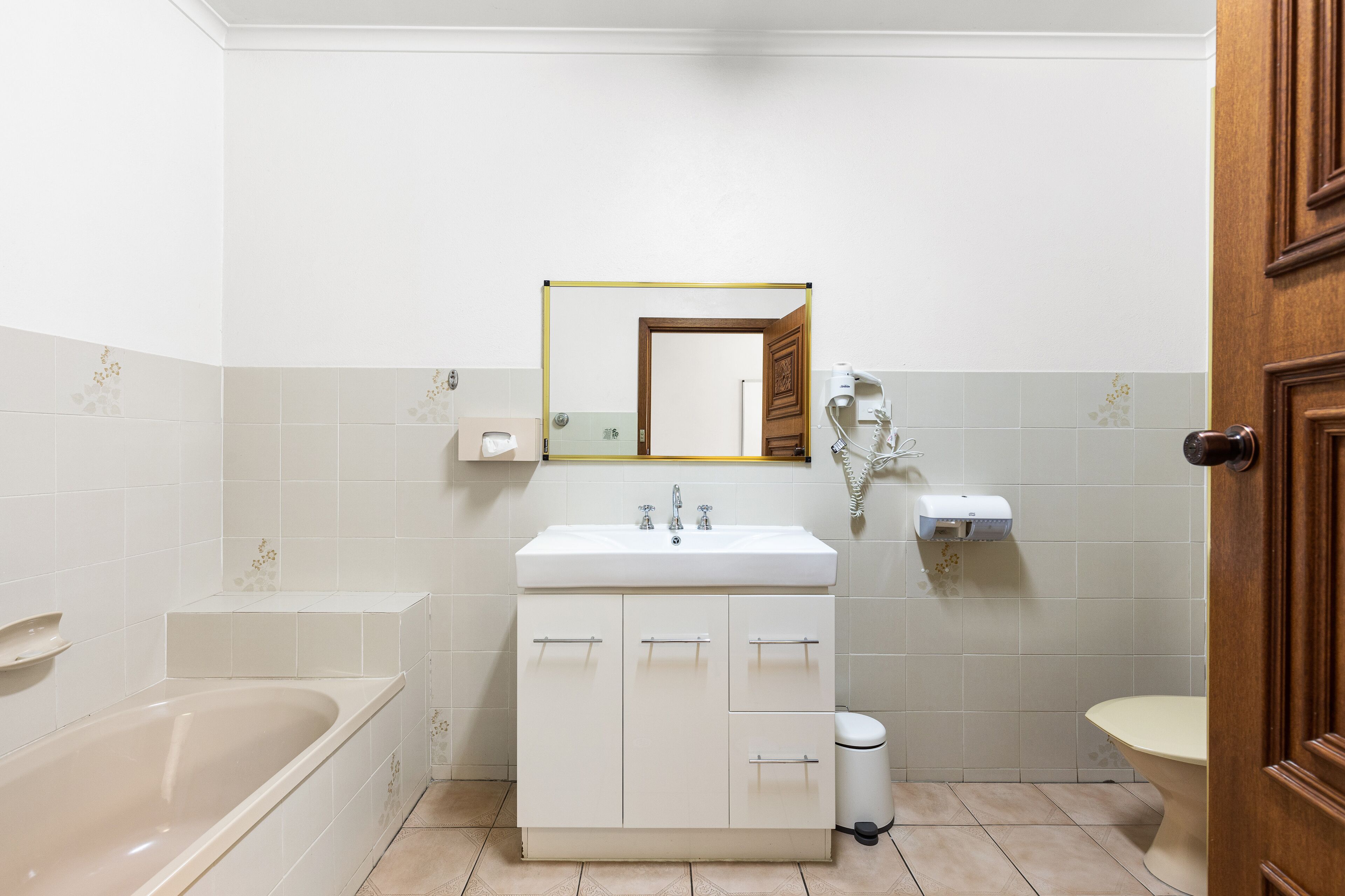 Et badeværelse med badekar, håndvask med spejl og toilet.