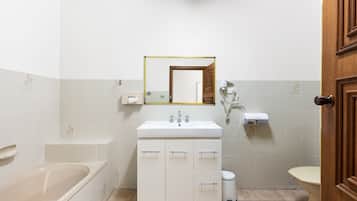 Et badeværelse med badekar, håndvask med spejl og toilet.
