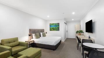Una habitación de hotel moderna con una cama, asientos tapizados en verde, un escritorio y una televisión.