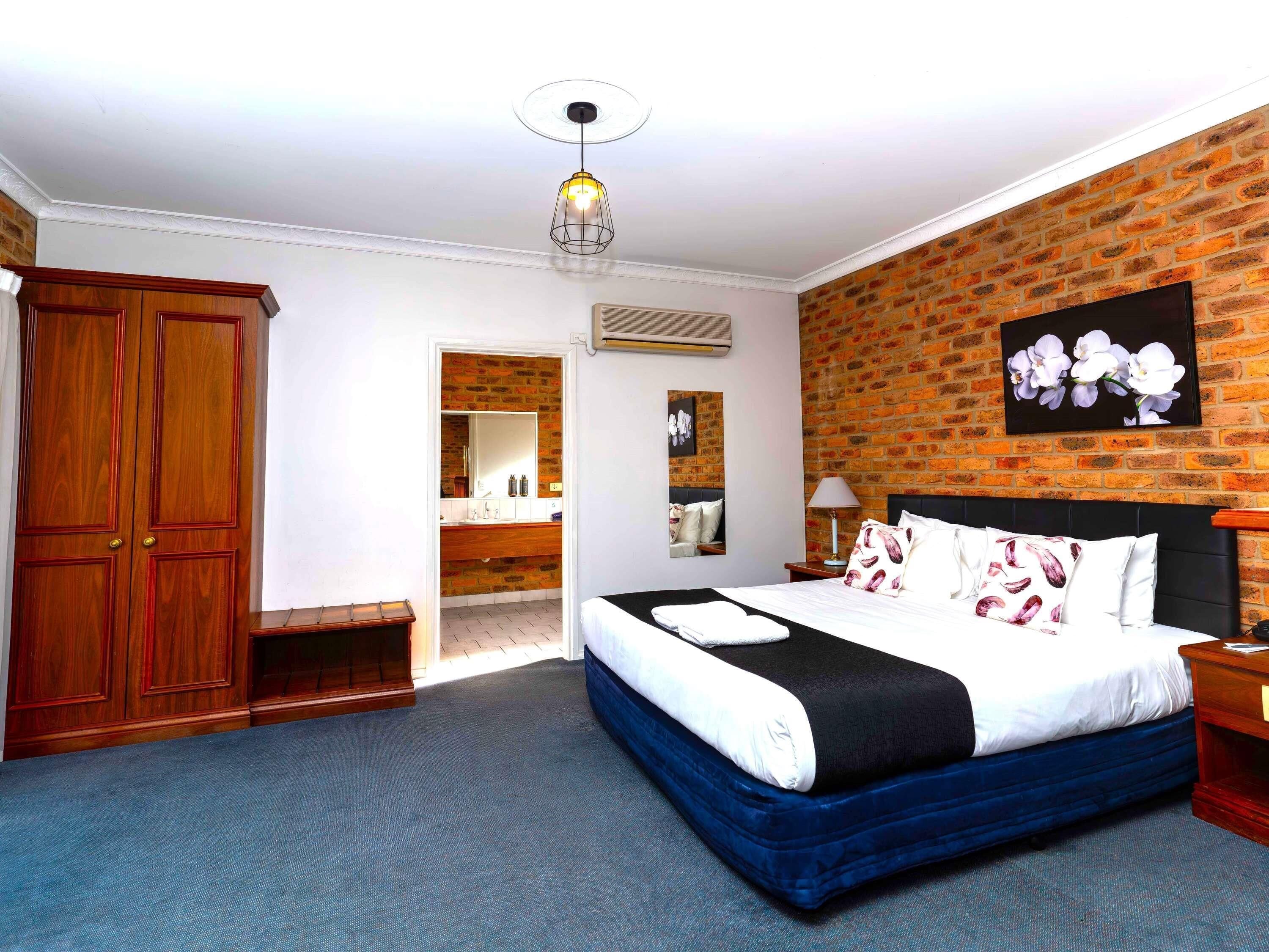 Een slaapkamer met een groot bed, een garderobe, een spiegel, een bakstenen muur en een plafondlamp.