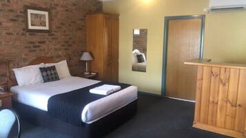 Ett hotellrum med en säng, en garderob i trä, ett nattduksbord, en lampa och en luftkonditioneringsanläggning.