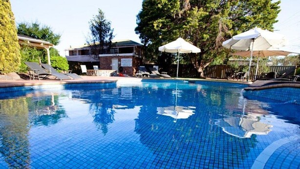 A swimming pool with tiled flooring, surrounded by lounge chairs and umbrellas. - Mercure Port of Echuca (Echuca)