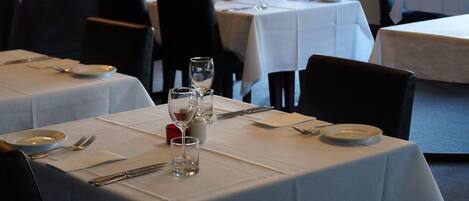 Un restaurante con mesas dispuestas para comer, con manteles blancos y vajilla sencilla.