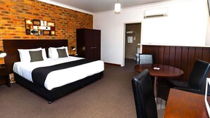 A hotel room with a brick-patterned wall, a bed, a wardrobe, a desk with a chair, and a small bathroom. - Mercure Port of Echuca (Echuca)