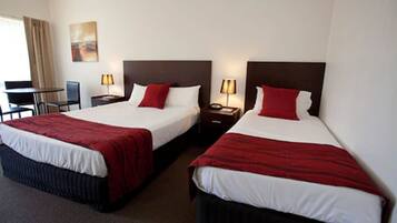 A hotel room with two beds, each with a red and white bedspread, a desk with a chair, a lamp, and a painting on the wall.