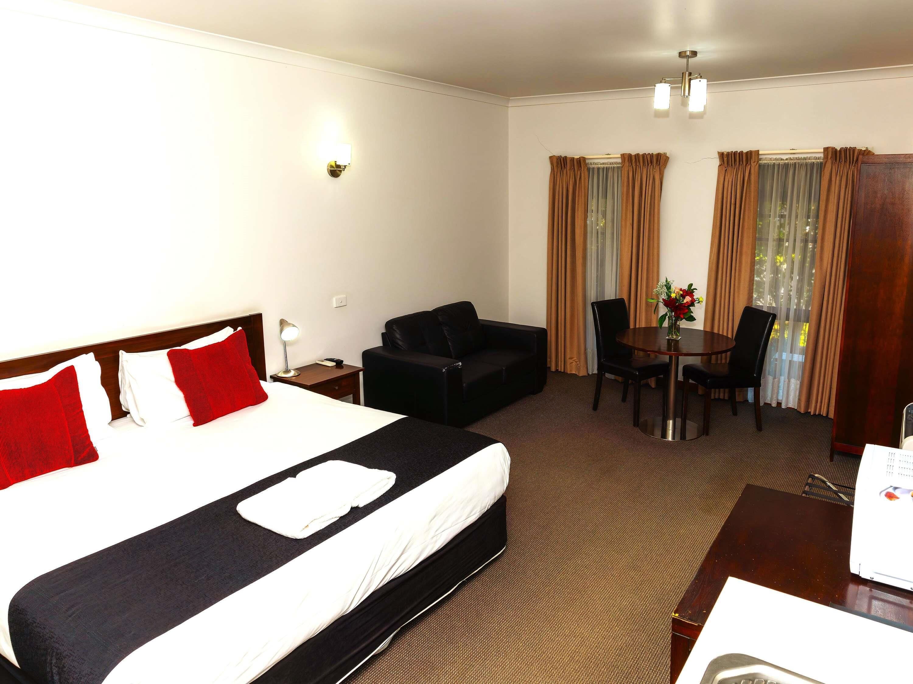 A hotel room with a bed, a desk, a chair, a table, and a window with curtains.
