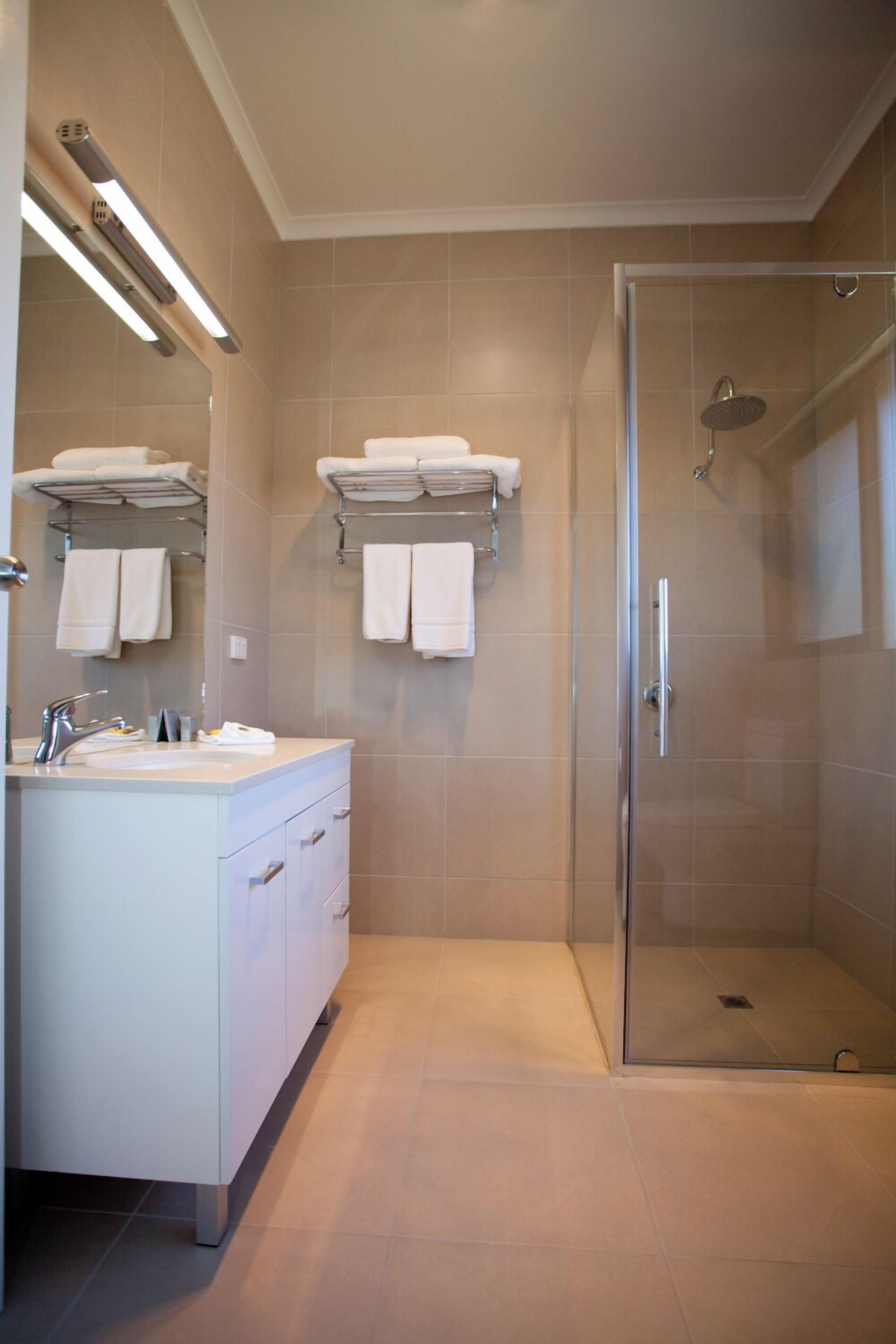 A modern bathroom with a glass-enclosed shower, a vanity with a mirror, and towel racks on the wall.