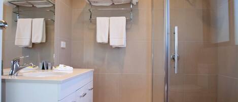 A modern bathroom with a glass-enclosed shower, a vanity with a mirror, and towel racks on the wall.