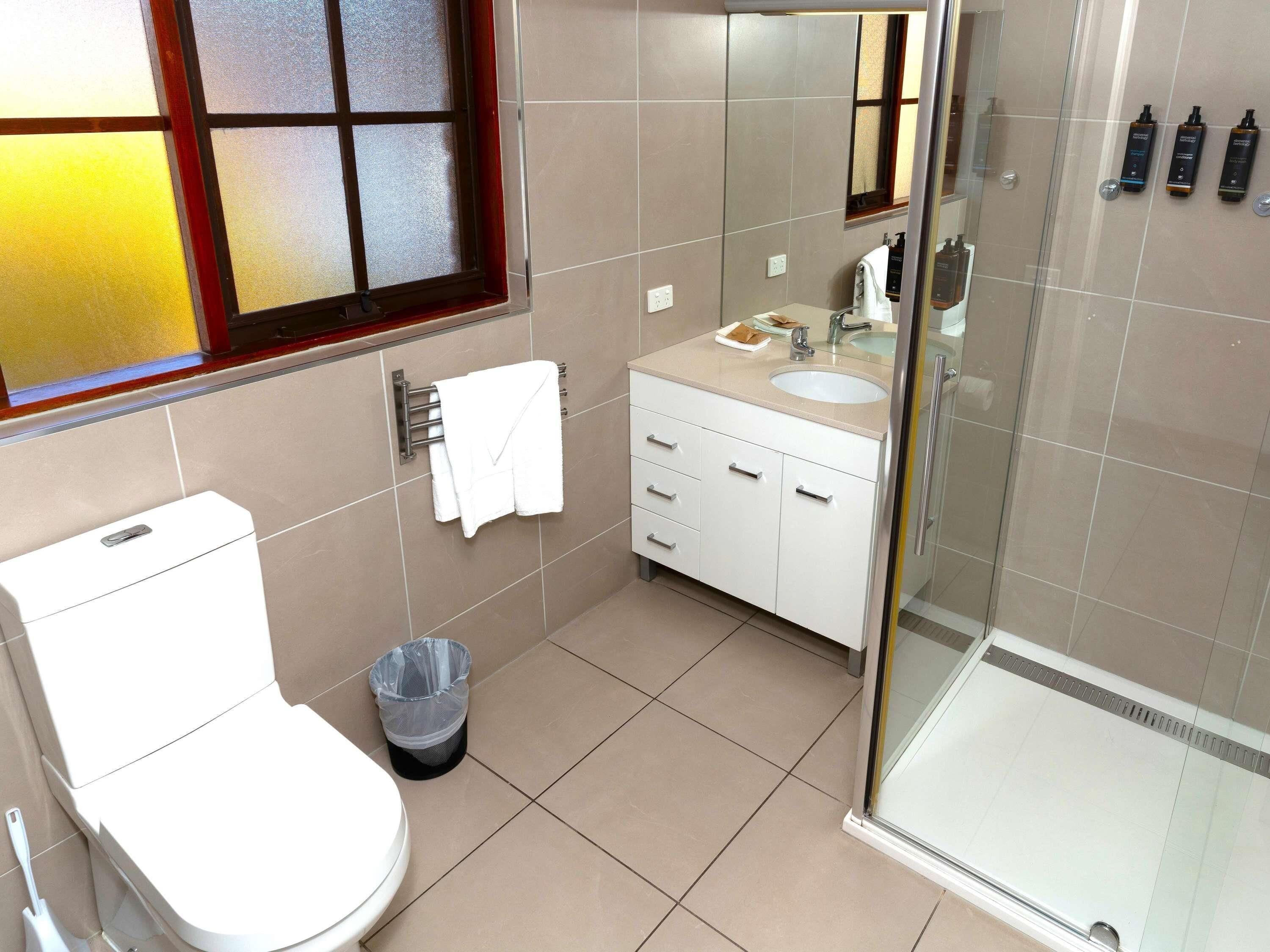 Une salle de bain comprenant des toilettes, un lavabo, un meuble-lavabo et une douche à parois de verre.