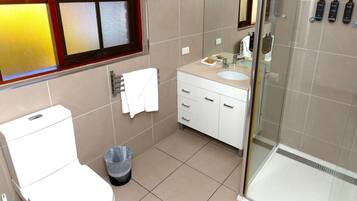 Une salle de bain comprenant des toilettes, un lavabo, un meuble-lavabo et une douche à parois de verre.