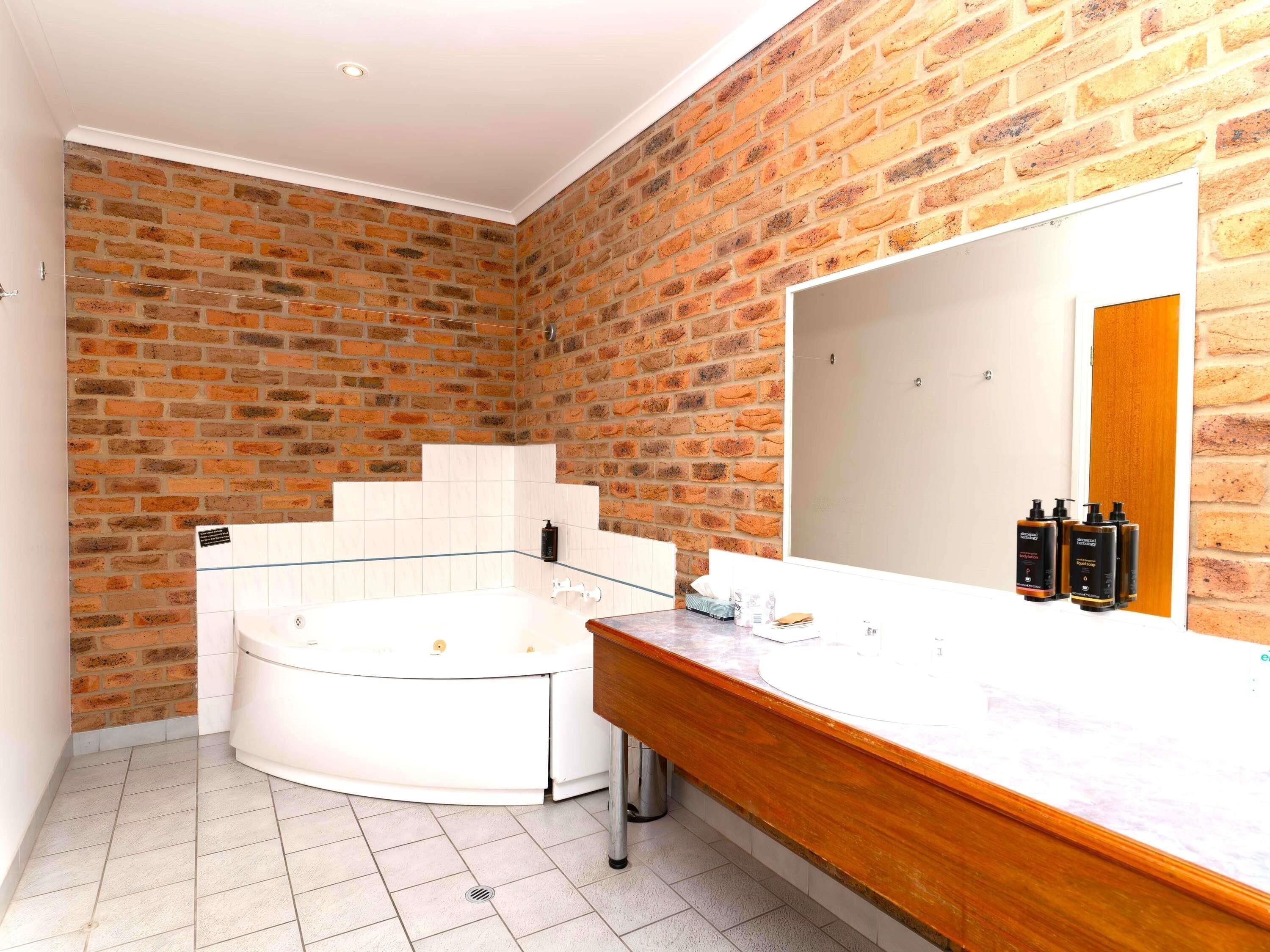 Une salle de bain avec un mur en briques, une baignoire blanche, un meuble-lavabo en bois et un grand miroir.
