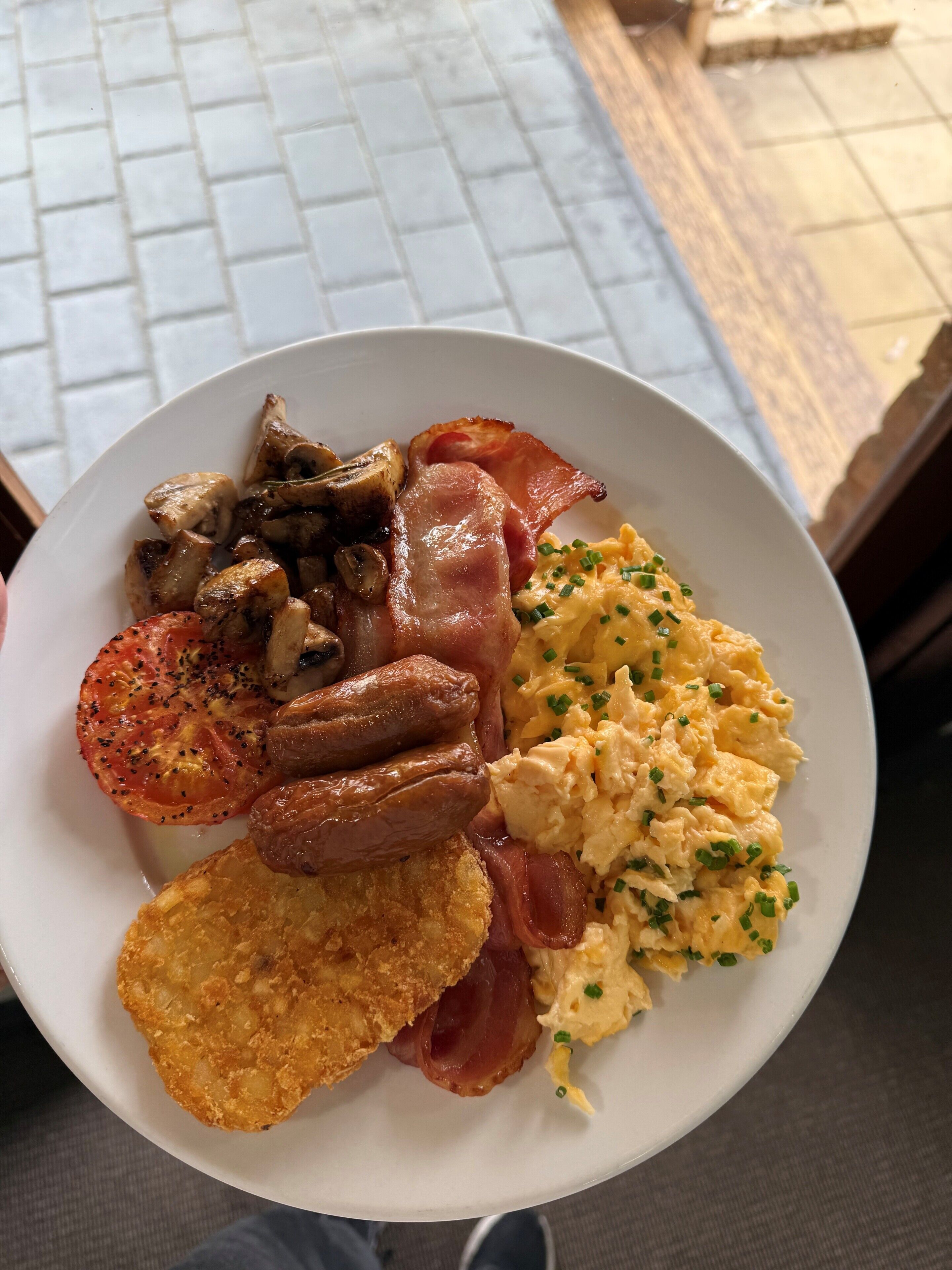 Un plato de comida con salchichas, champiñones, tomates, huevos revueltos y tostadas.