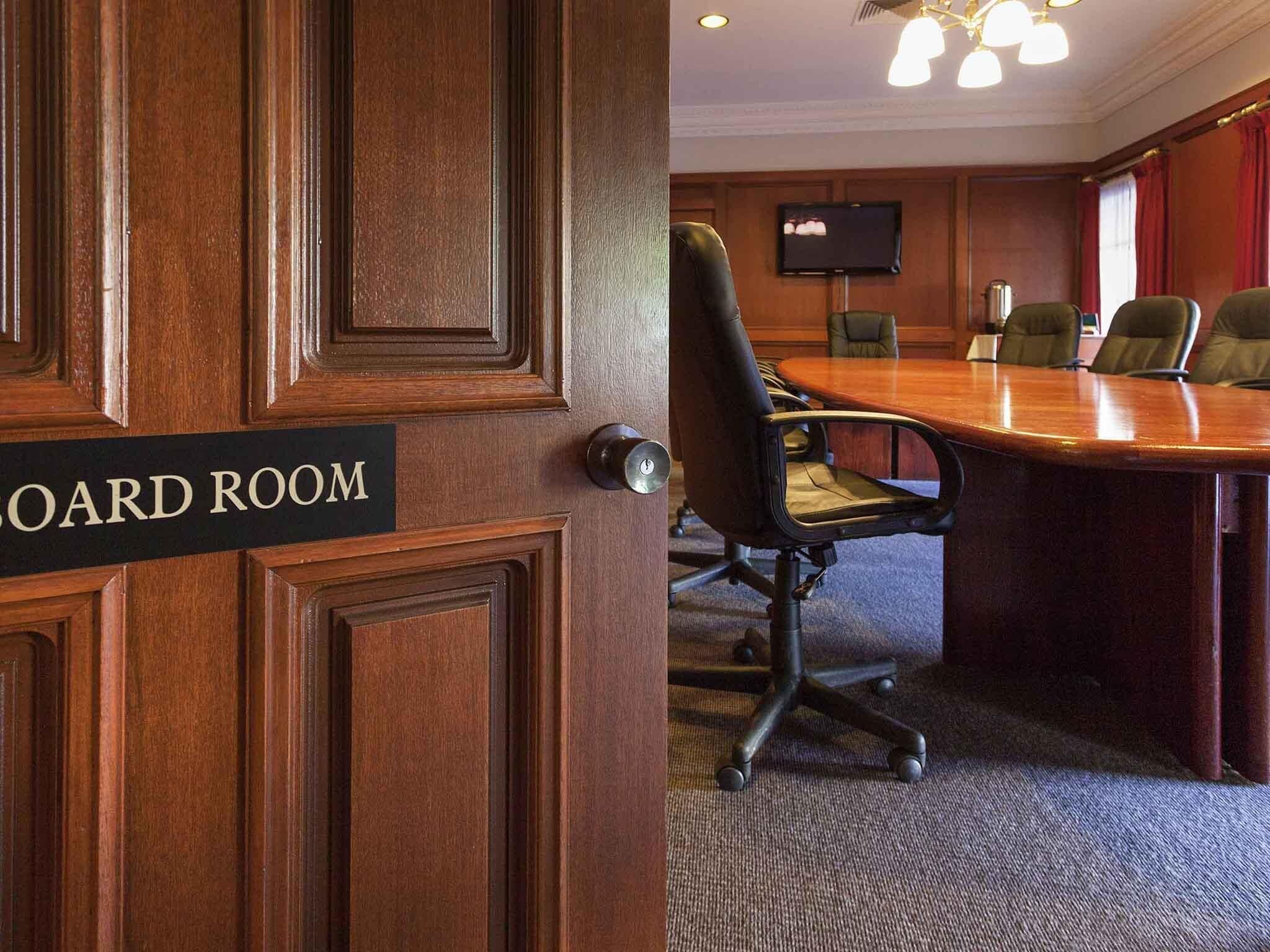 A conference room with a wooden door labeled 'BOARD ROOM,' a large table, and several chairs.