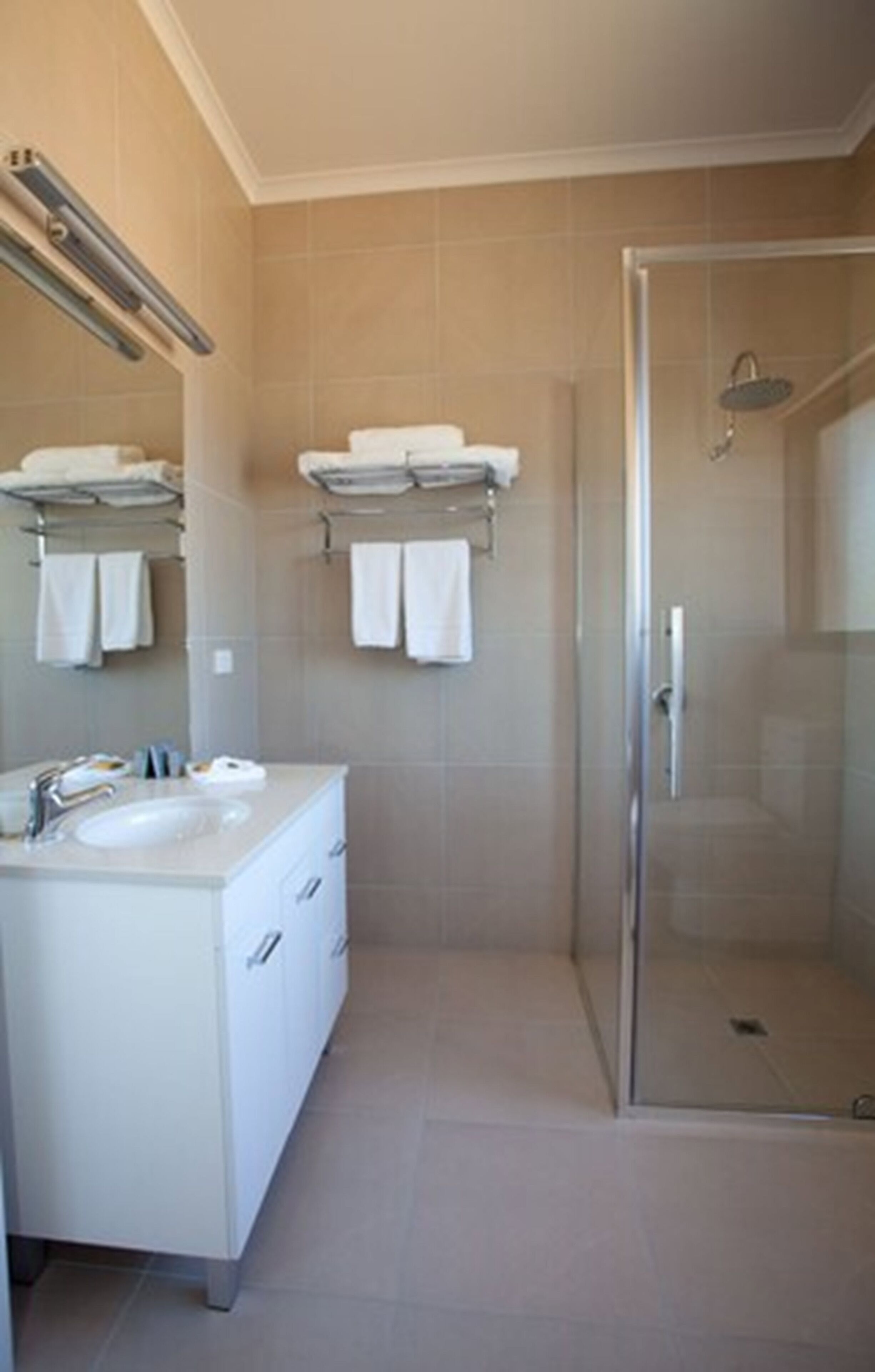 Un baño moderno con ducha de vidrio, tocador blanco con lavamanos y varios ganchos para toallas.
