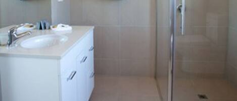 Un baño moderno con ducha de vidrio, tocador blanco con lavamanos y varios ganchos para toallas.
