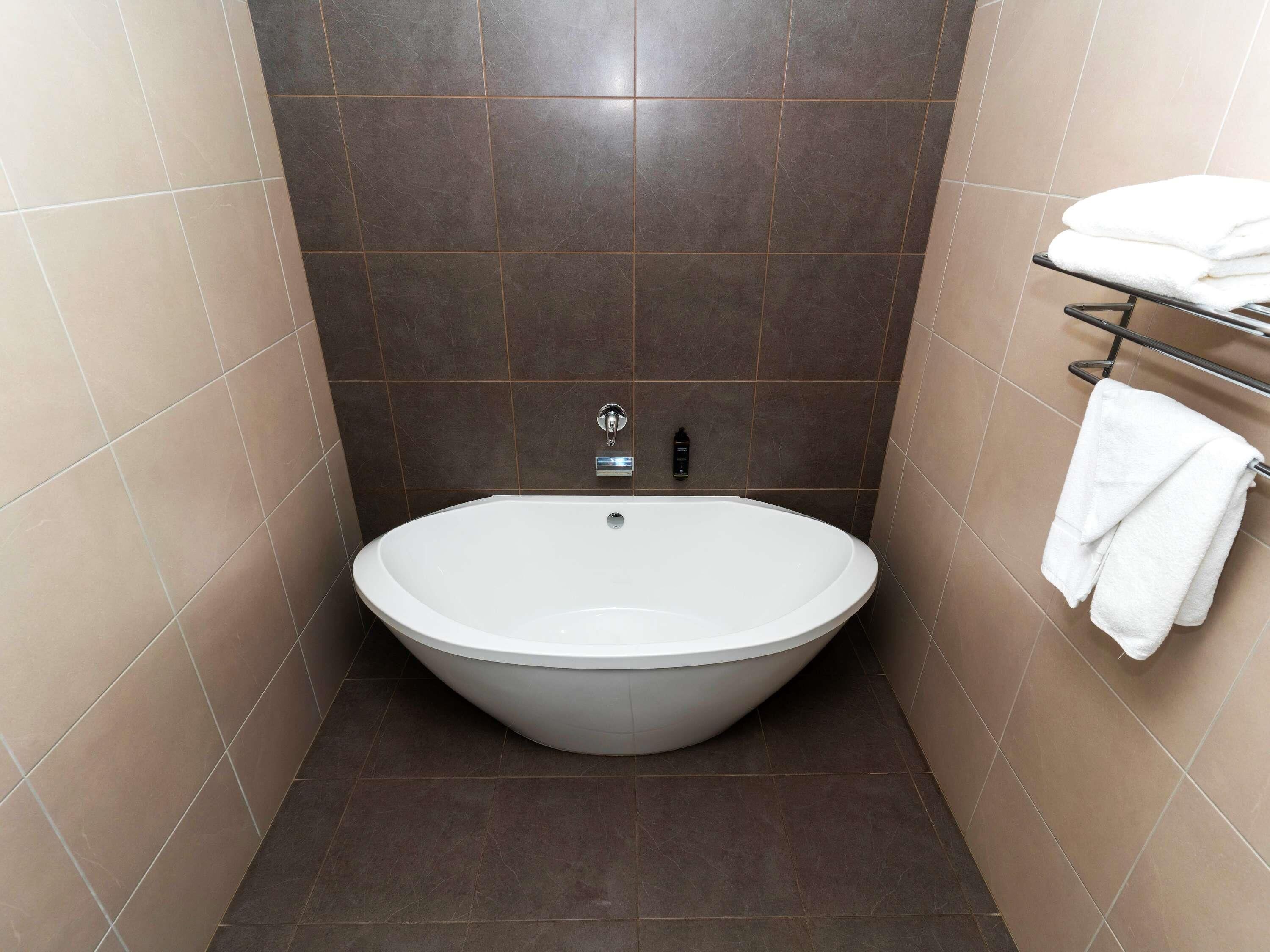 A bathroom with a freestanding bathtub, a towel rack with towels, and a wall-mounted faucet.